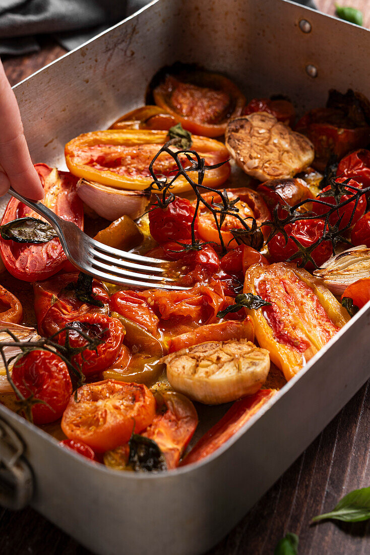 Fork pressing on baked fresh tomatoes, garlic, shallots, basil