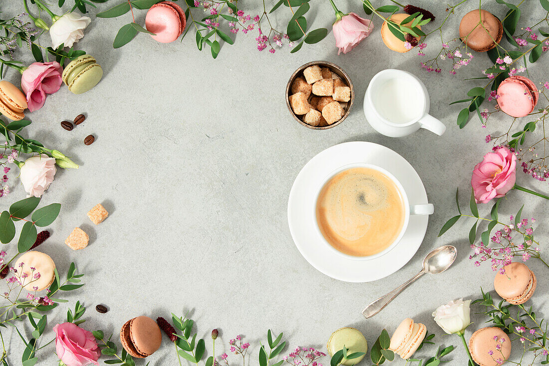 White coffee cup and frame made of spring flowers and different types of macaroons. Flat lay mock up copy space