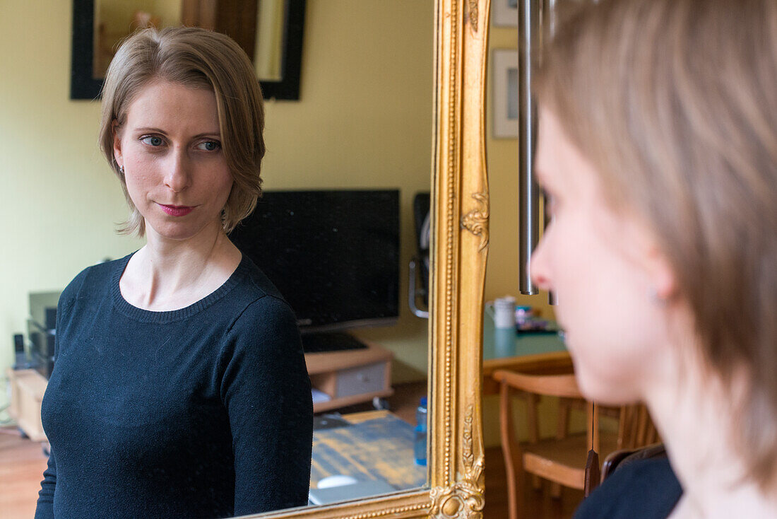 Tilburg, Netherlands. Young adult caucasian woman watching herself in a living room mirror after doing her make up.