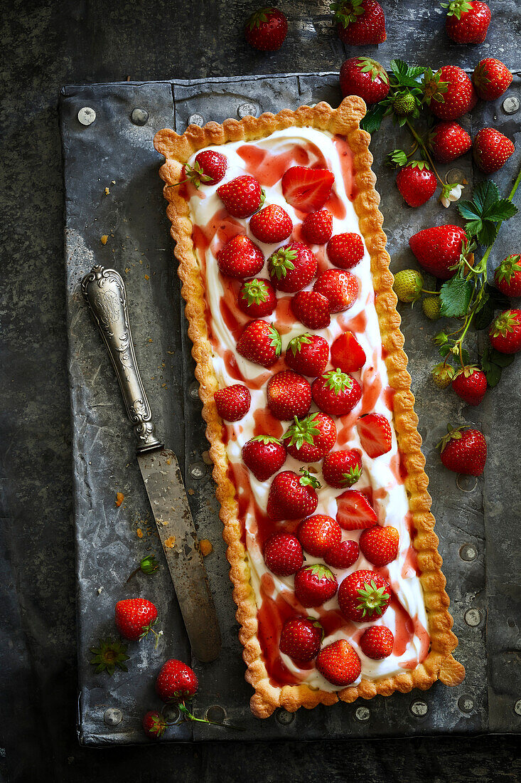 Homemade square strawberry tartlet filled with cream, fresh strawberries and strawberry syrup on a grey metal surface