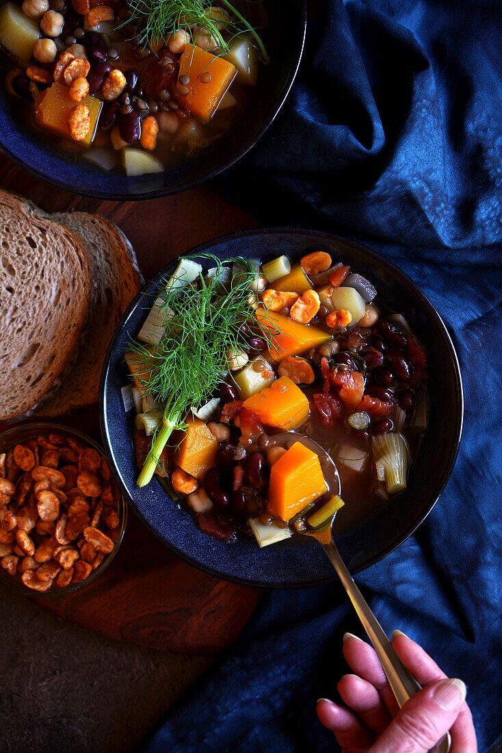 Sardinian-style minestrone longevity soup served with sourdough bread and roasted fava beans. Close up with female hand.