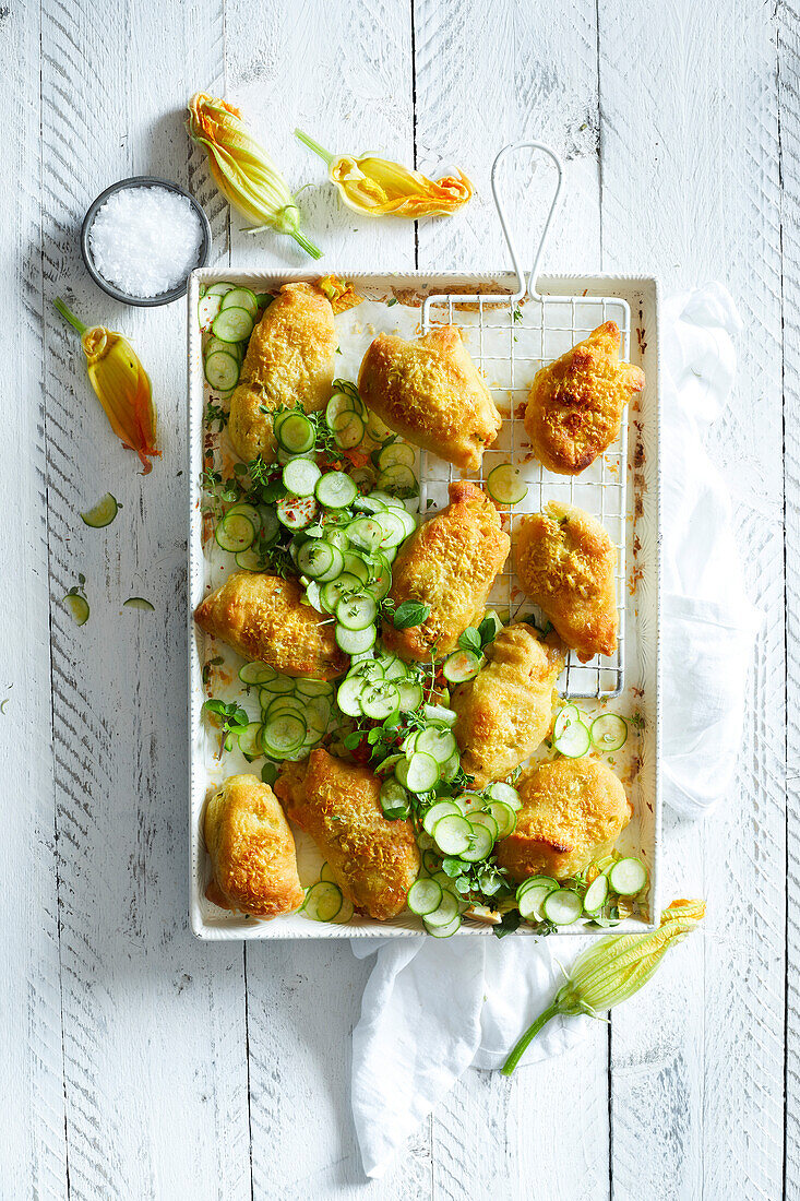 Gebackene Zucchiniblüten auf einem weißen Backblech, serviert mit Mini-Zucchinischeiben auf weißem Holzhintergrund