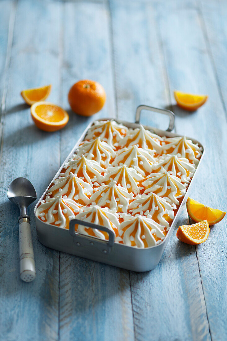 Hausgemachtes frisches Vanille-Orangeneis-Dessert mit Baiserstücken auf blauem Holzhintergrund