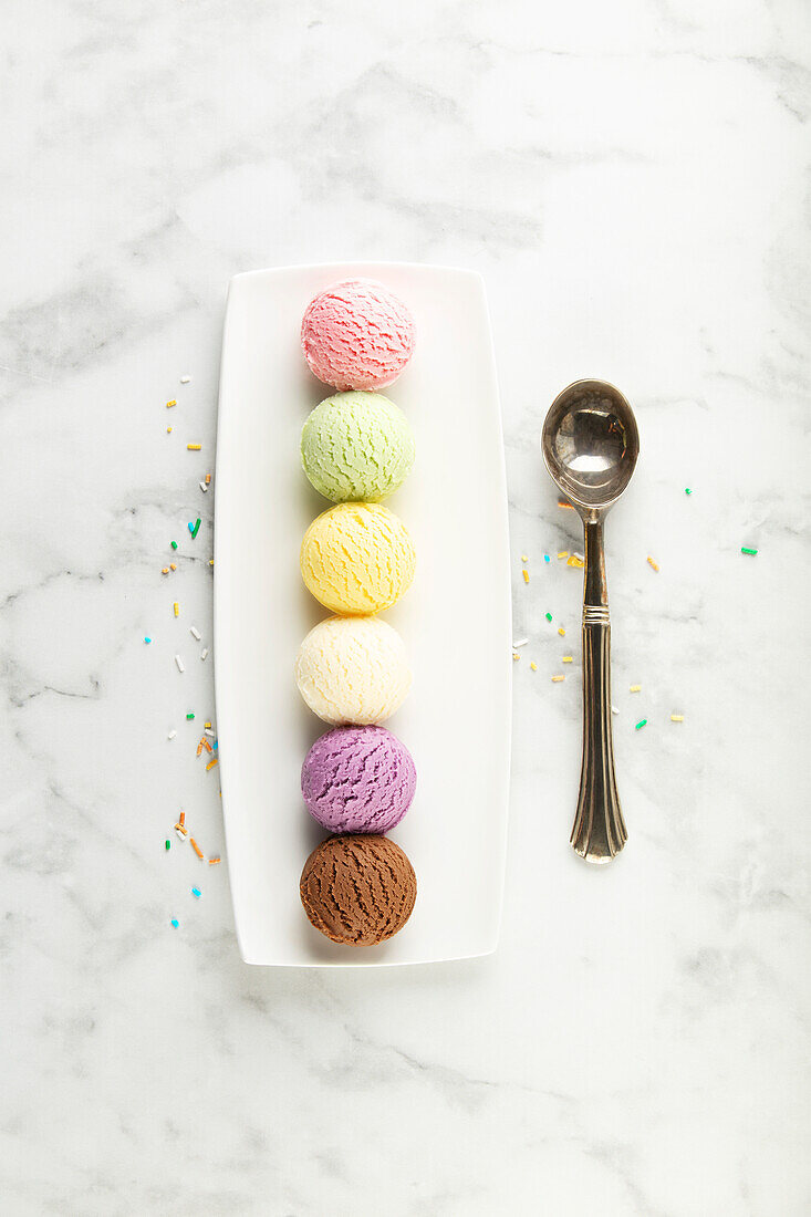 Assorted ice cream scoops on white marble background. Strawberry, pistachio, mango, vanilla, blueberry and chocolate ice cream. Top view, laid flat