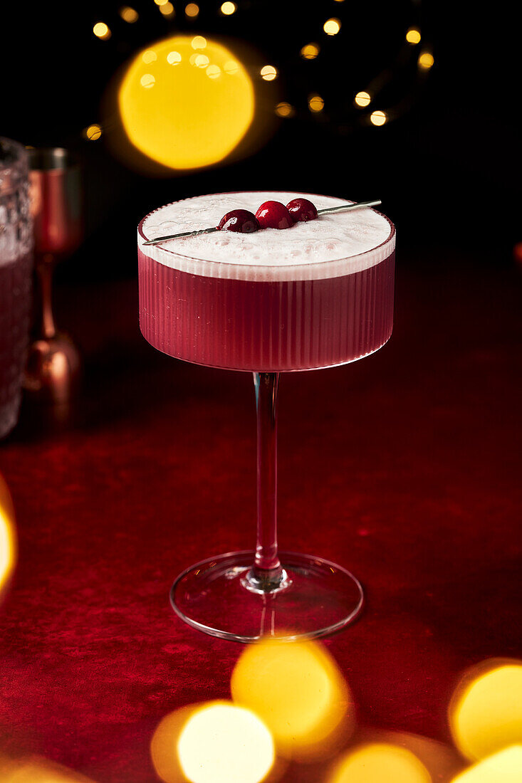 Mulled wine sour with cranberries on a red surface with fairy lights and glasses