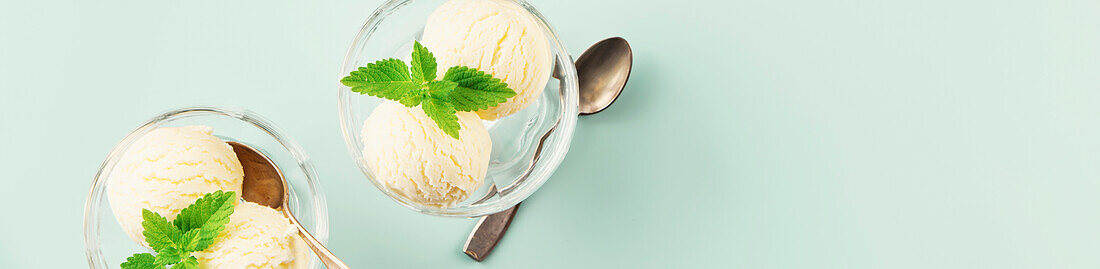 Scoops of Vanilla and mint leaves in glass bowl over pastel light blue background, top view, banner, copy space. Summer minimal concept