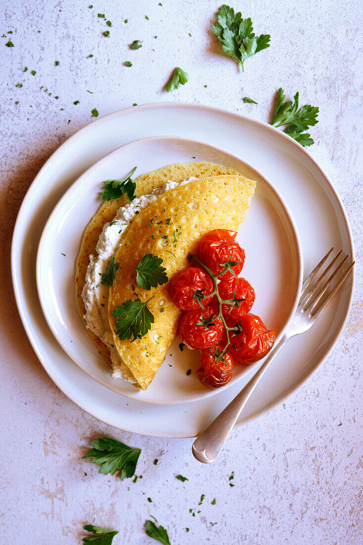 Glutenfreie Crepes mit Kräuter-Ricotta und gebratenen Rispentomaten. Nahaufnahme.