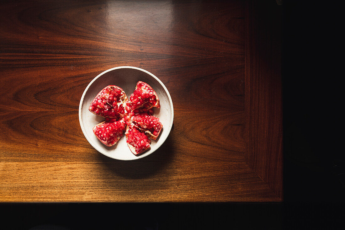 Pomegranate in a ceramic bowl on a wooden table.