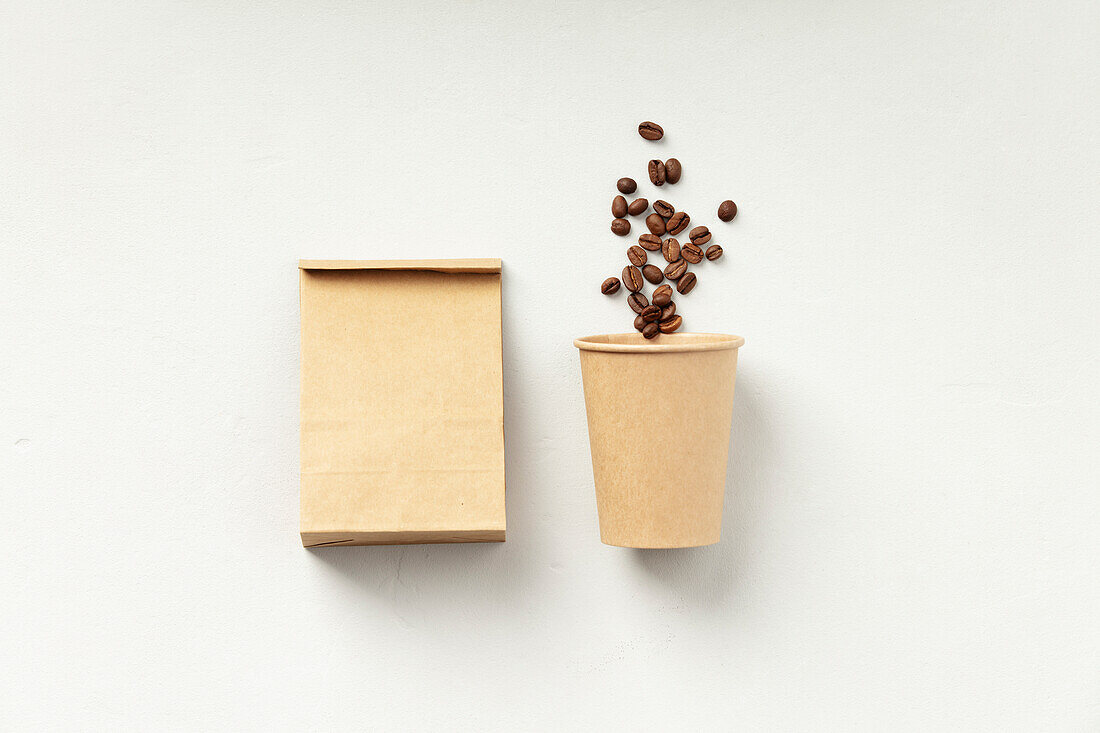 A paper coffee cup next to a brown bag of coffee beans on a white background.