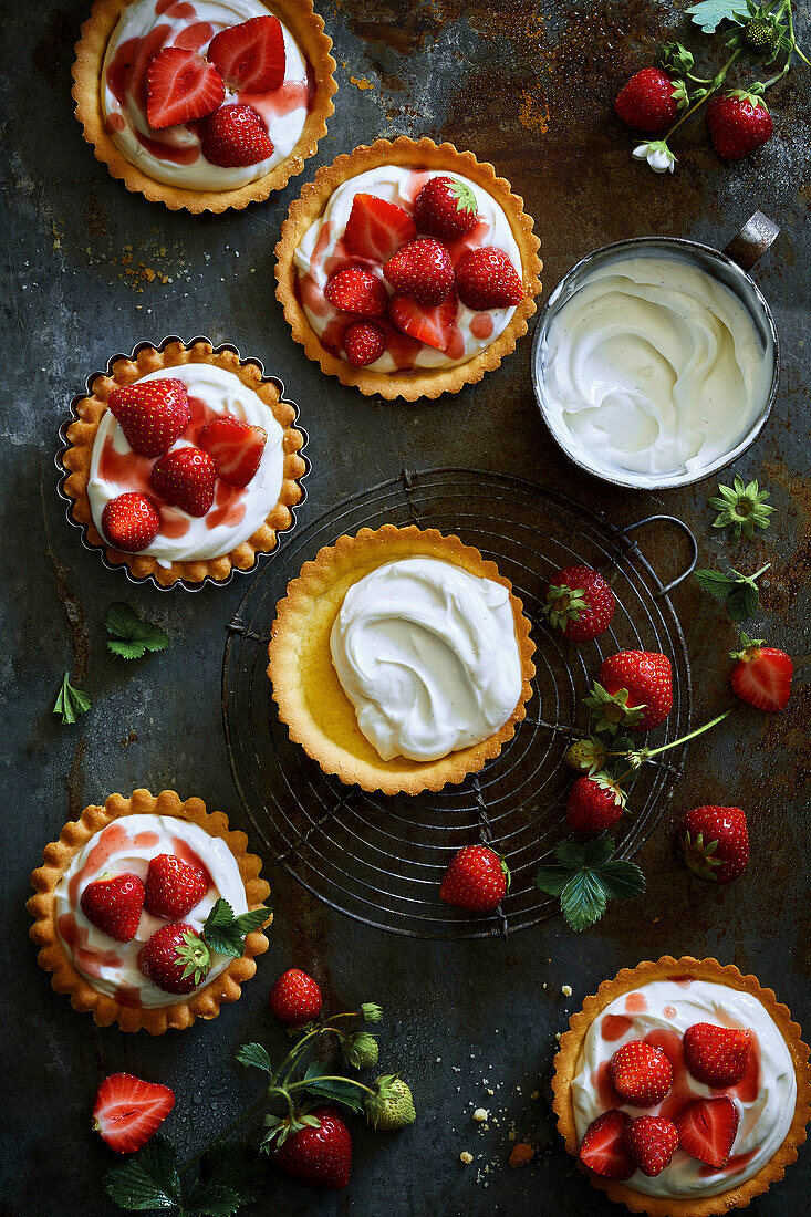 Hausgemachte runde Erdbeertörtchen, gefüllt mit Sahne, frischen Erdbeeren und Erdbeersirup auf grauem Metallhintergrund