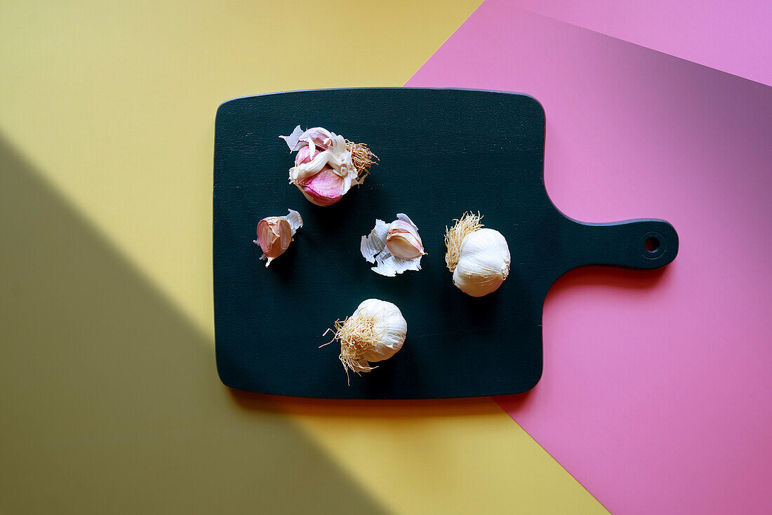 Garlic bulbs on a cutting board with a colour block and geometric shadow aesthetic.