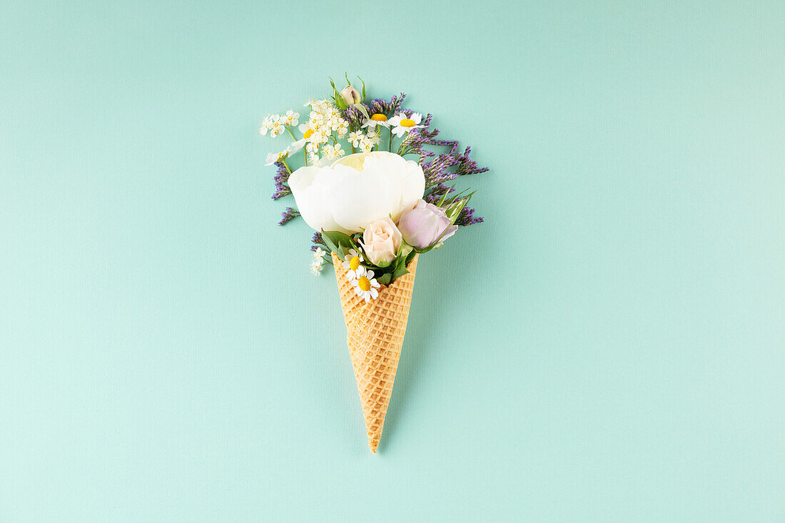 Creative still life of waffle cone with flowers over pastel light blue background, top view. Summer minimal concept