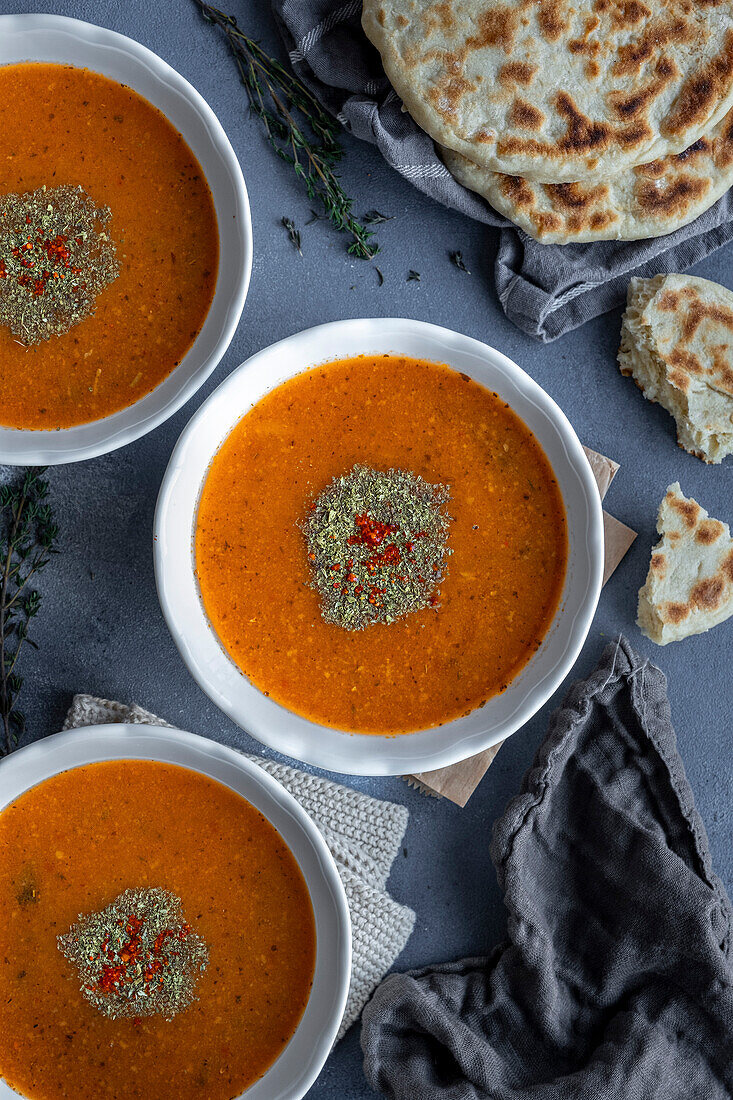 Tarhana soup in three white bowls, garnished with dried mint and red paprika flakes, served with Turkish flatbread.