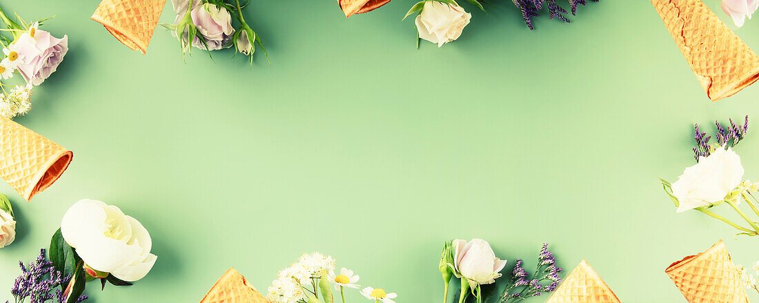 Flat lay of waffle cones and flowers on a pastel green background, top view, flat lay. Spring or summer mood concept, banner, copy space