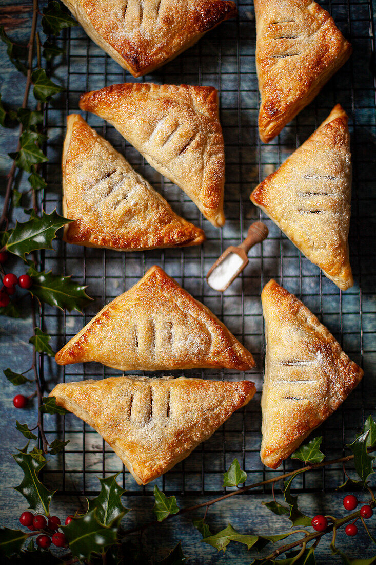 Fruit turnovers made with puff pastry on a wire rack surrounded by holly.