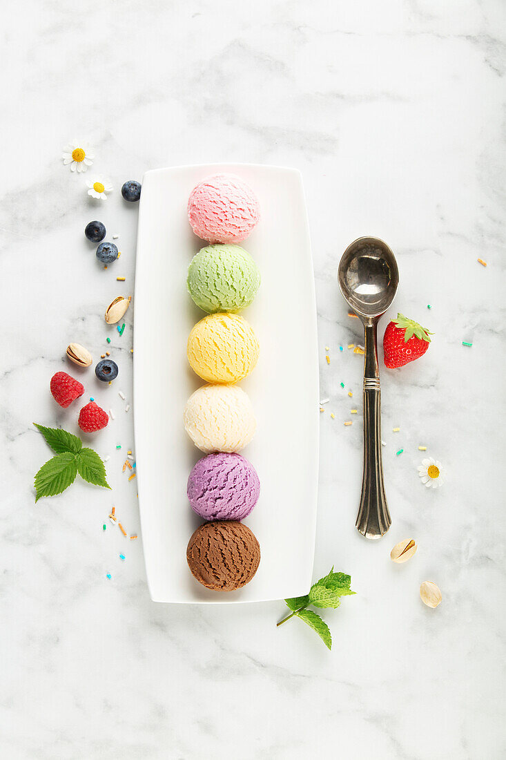 Various scoops of ice cream and berries on a white marble background. Strawberry, pistachio, mango, vanilla, blueberry and chocolate ice cream. Top view, laid flat.