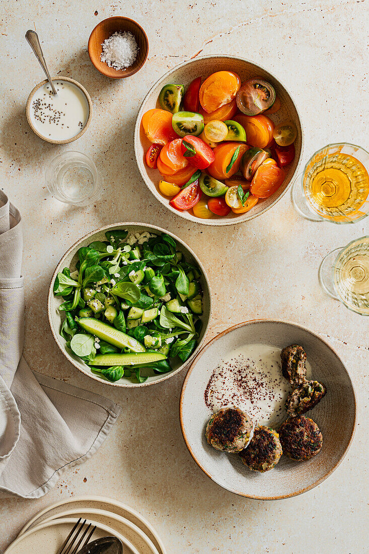 Wide flatlay tablescape of mezze dishes in soft light on a stone background