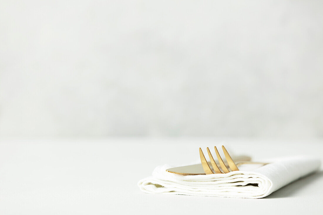 Golden Cutlery set and white napkin on light grey table with space for text. Festive table setting