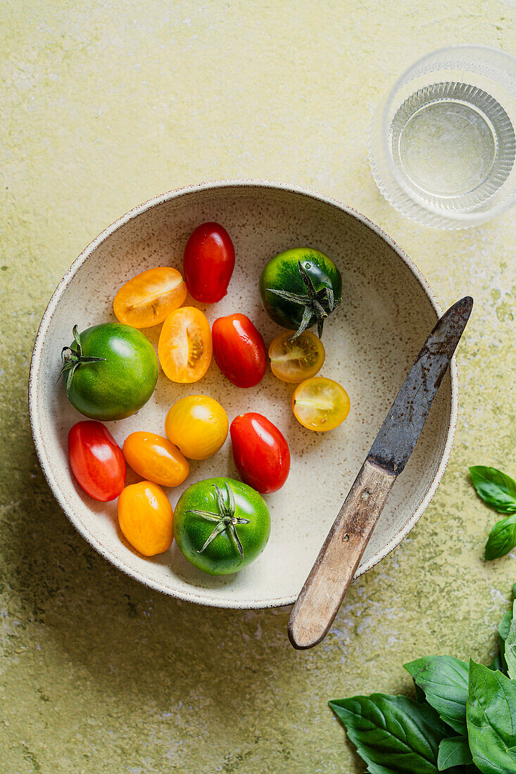 Bowl of small, coloured charry and plum tomatoes with a small knife on green background