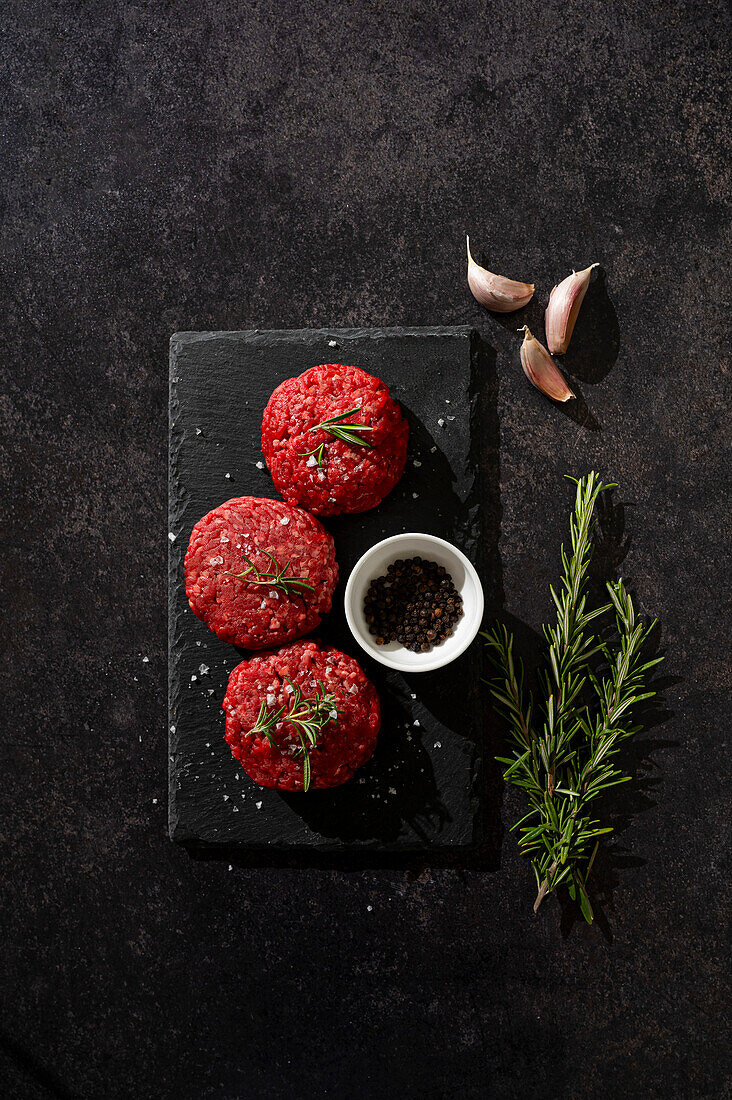 Rindfleisch-Burger-Patties auf einer schwarzen Schieferplatte