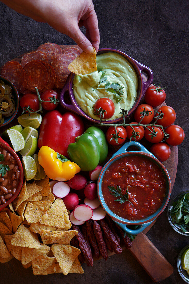 Mexican charcuterie board with dips, salsa, beans, jalapeños, chorizo and tortilla chips. Guacamole for hand dipping.