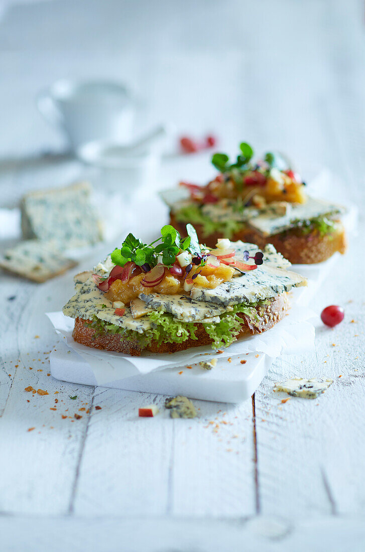 Two slices of baguette topped with blue cheese, chutney, grapes, apples and water cress