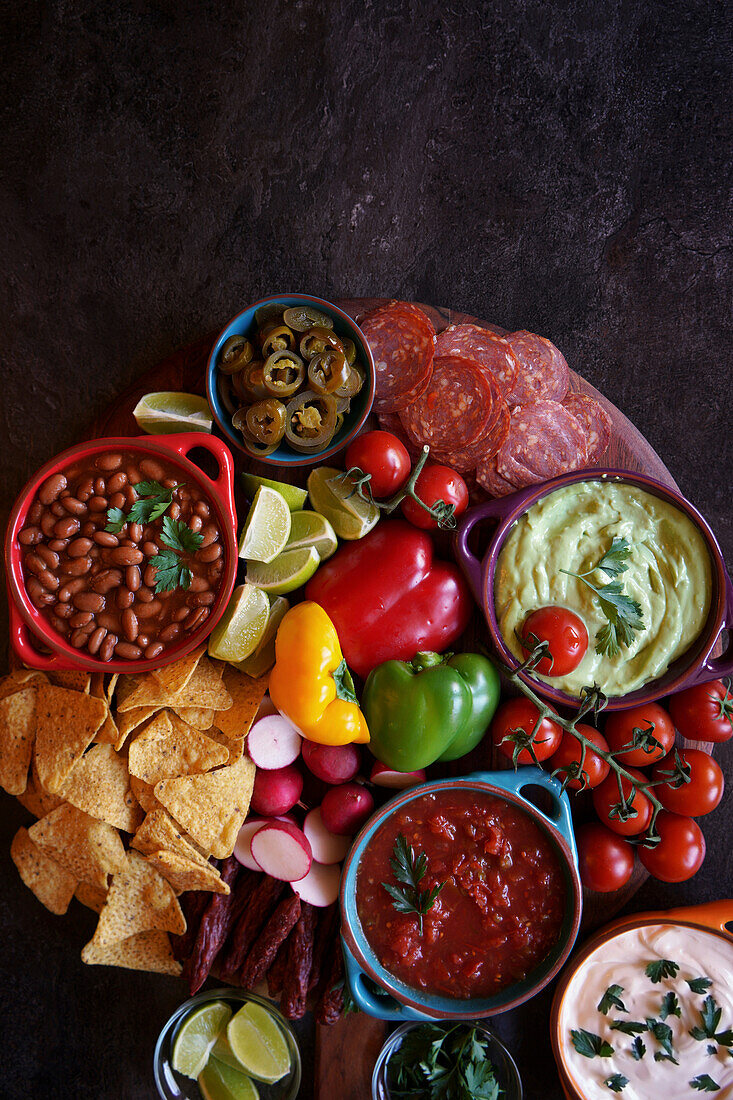 Mexican charcuterie board with guacamole, salsa, beans, jalapenos, chorizo and tortilla chips. Negative copy space.