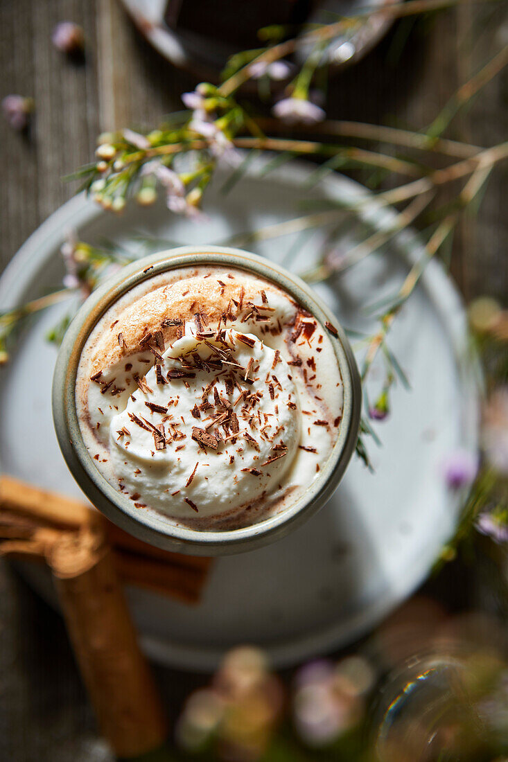 Mexikanische heiße Schokolade mit Schlagsahne auf einem dunklen Holzhintergrund mit Blumen, Keksen und Zimtstangen.