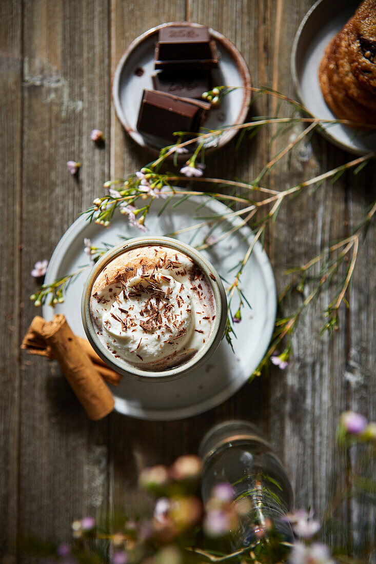 Mexikanische heiße Schokolade mit Schlagsahne auf einem dunklen Holzhintergrund mit Blumen, Keksen und Zimtstangen.