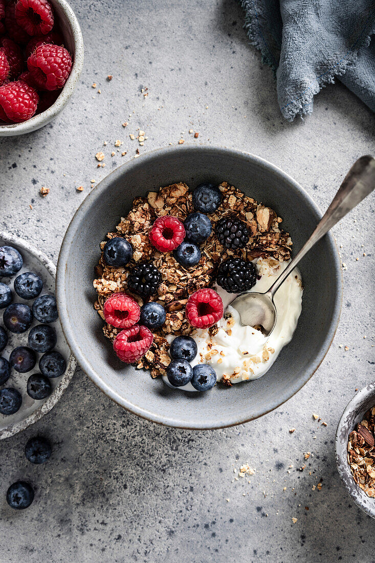 Granola with raspberries, blueberries, blackberries and yoghurt on a grey background