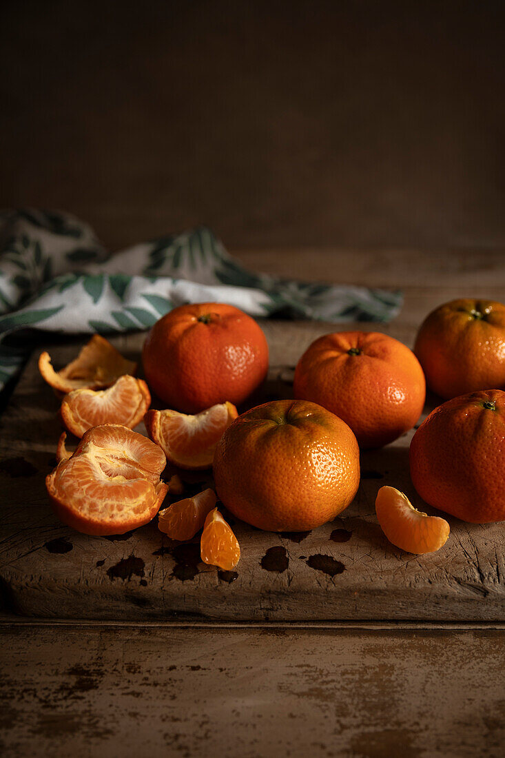 Fresh mandarins on a wooden table with green linen against a dark background.