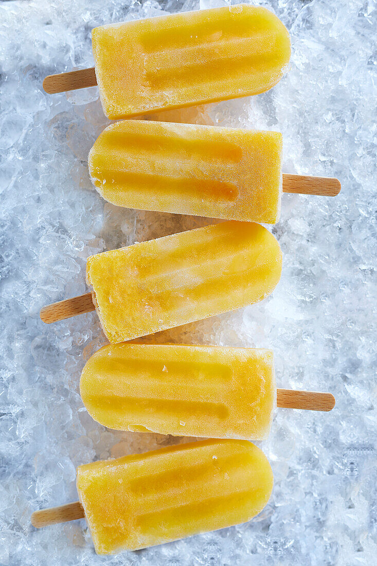 Homemade ice-cold orange popsicles on crushed ice