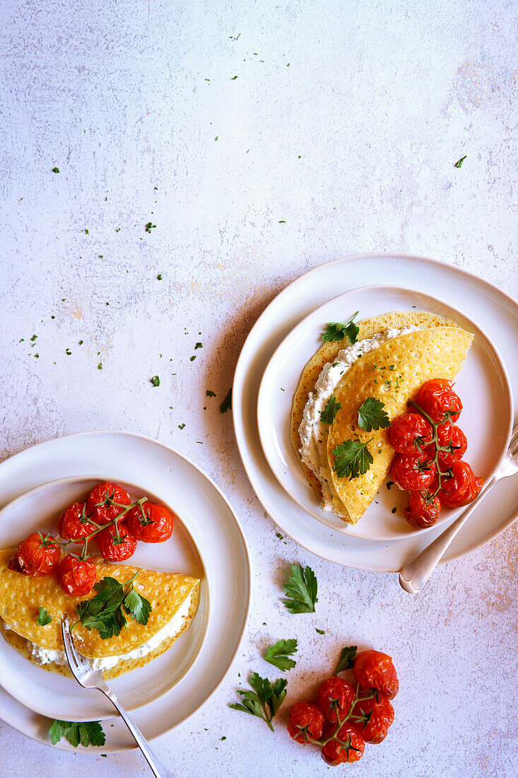 Glutenfreie Crepes mit Kräuter-Ricotta und gebratenen Rispentomaten. Negativer Kopierraum.