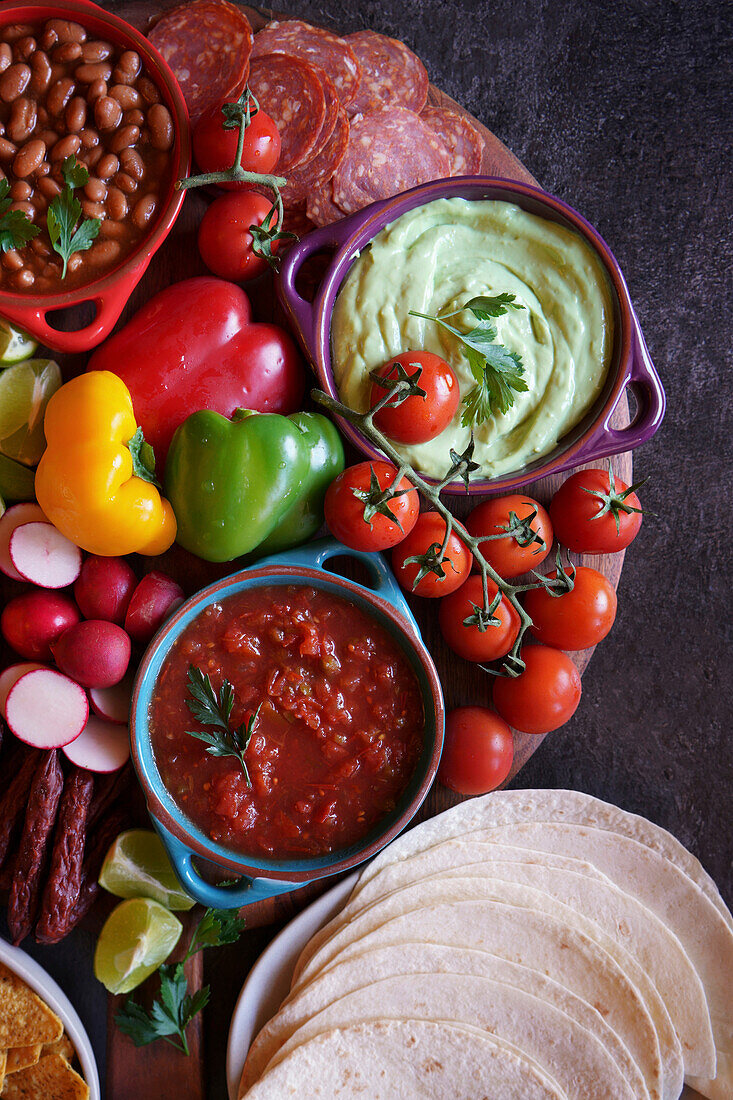 Mexican sausage platter with guacamole, salsa, beans, jalapeños and chorizo. Close-up with tortillas.