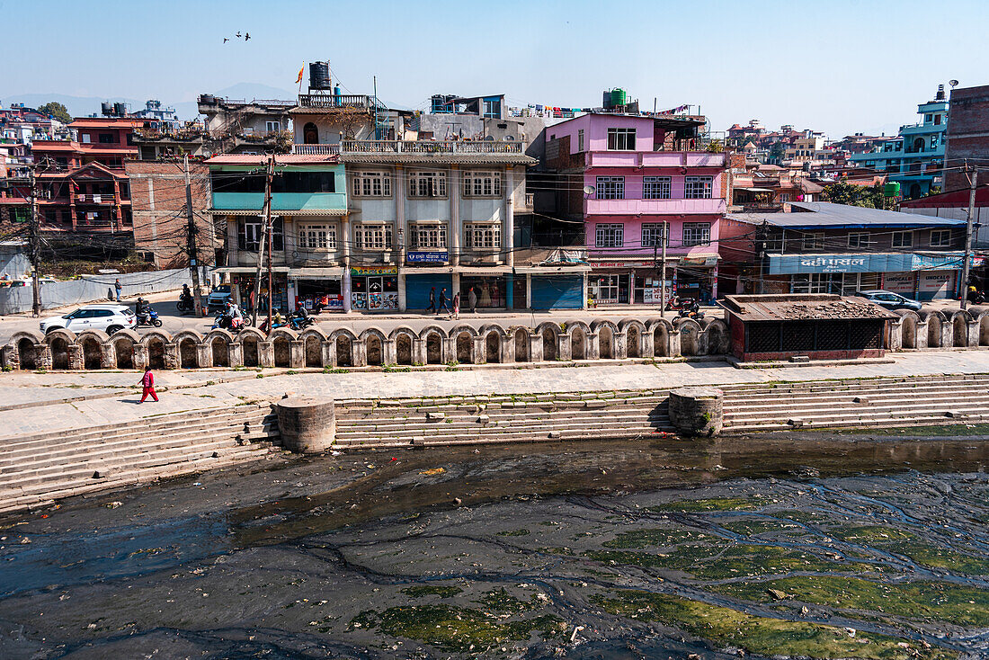 Blick über das verschmutzte Wasser des heiligen Bagmati-Flusses vor typischen nepalesischen Häusern, Pashupatinath, Kathmandu, Nepal, Asien