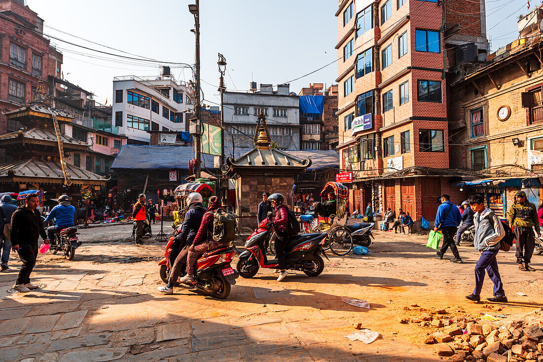 Busy traffic of motor bikes and pedestrians on a dusty market road, warm light of the morning rush hour, Kathmandu, Nepal, Asia