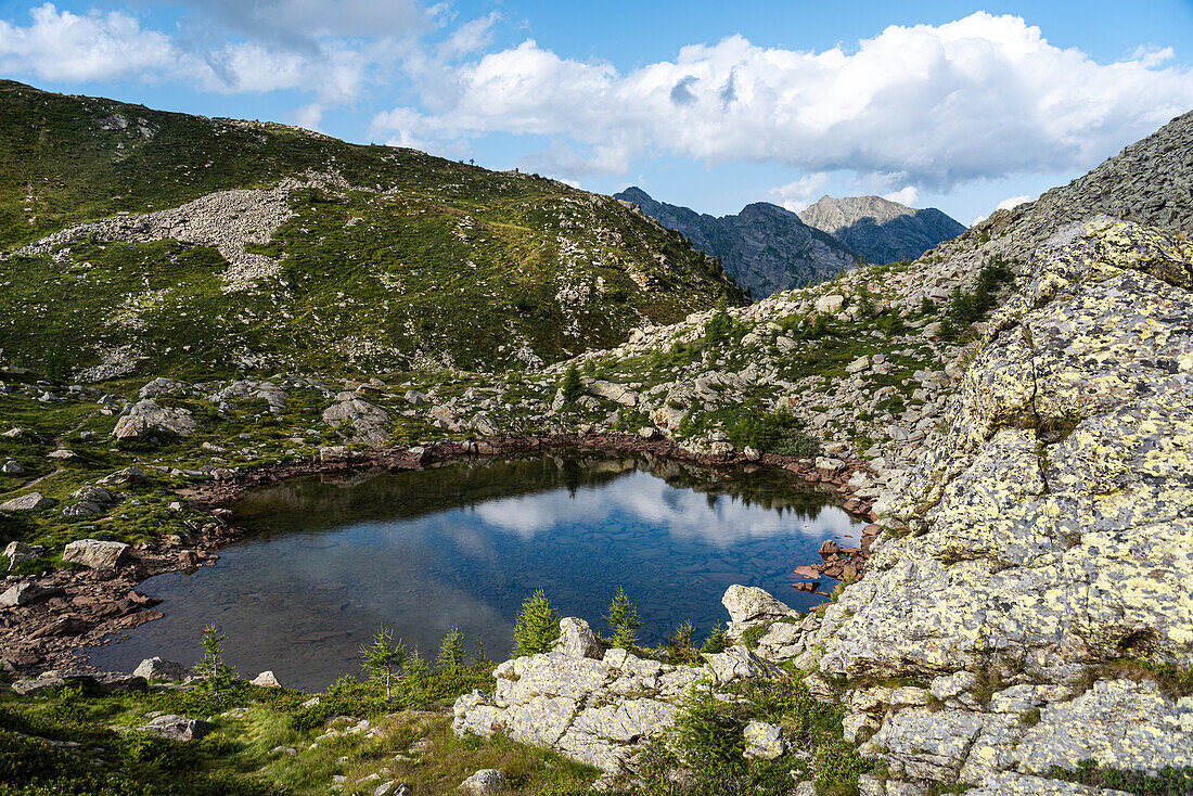 Blick hinunter auf einen unberührten Bergsee, umgeben von felsigen und grasbewachsenen Bergen an der natürlichen Grenze zwischen der Schweiz und Italien, Cima Verosso, Piemont, Italien, Europa