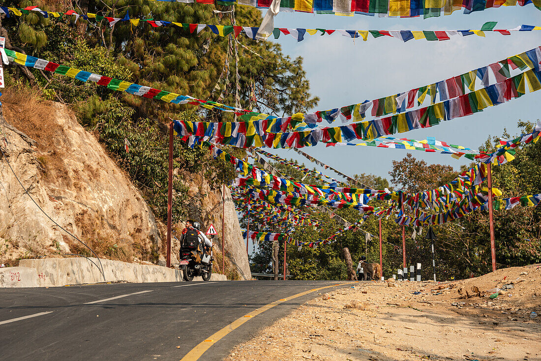 Nepalesische Gebetsfahnen über einem Highway mit einem vorbeifahrenden Motorrad, Kathmandutal, Nepal, Asien