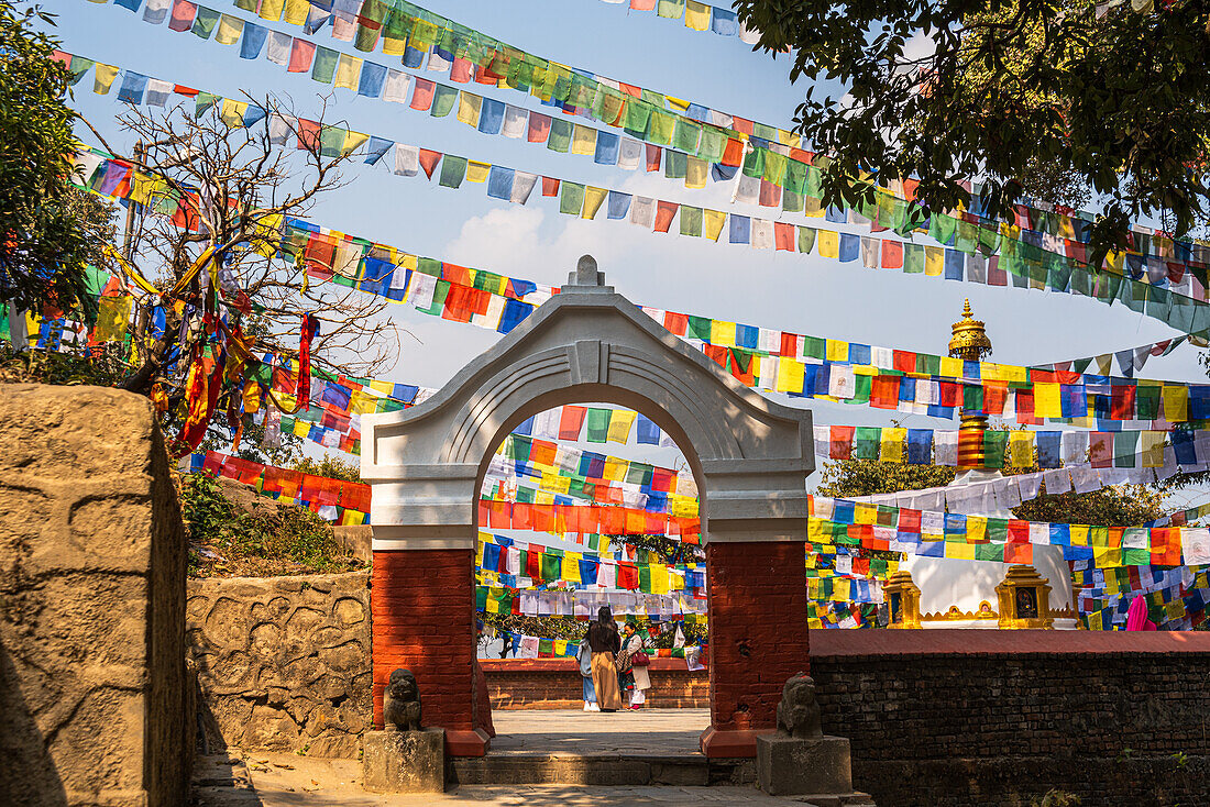 Steinbogentor, das zur Kashyap Stupa führt, mit bunten buddhistischen Gebetsfahnen, Kathmandu, Nepal, Asien