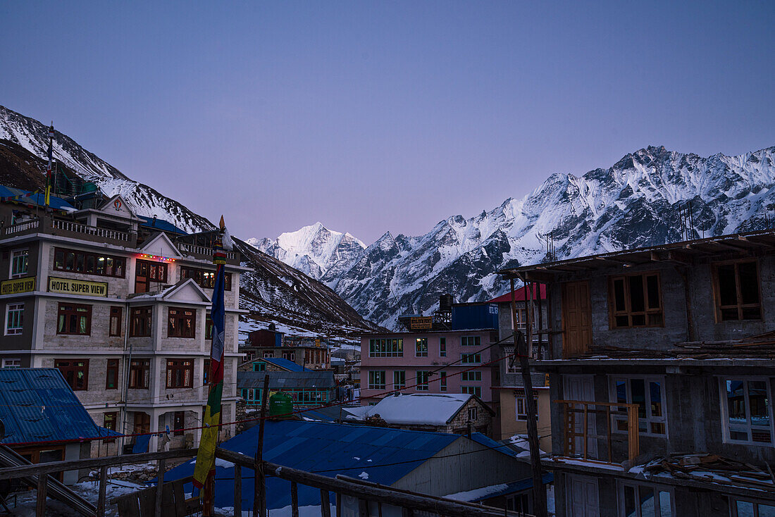 Blick über die Stadt Kyanjin Gompa mit weichem violettem Licht nach Sonnenuntergang und dem verschneiten Gipfel des Gangchempo, Lang Tang Valley Trek, Himalaya, Nepal, Asien