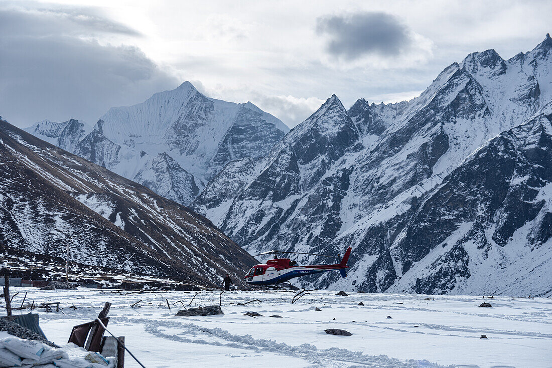 Helicopter landing on a snowy field in front of high altitude mountain landscape with Gangchempo summit, Langtang Valley Trek, Himalayas, Nepal, Asia