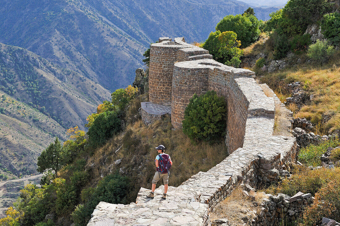 Young woman standing on a defensive wall of Smbataberd Fortress, on the crest of a hill between the villages of Artabuynk and Yeghegis, near Yeghegnadzor, Vayots Dzor province, Armenia, Eurasia