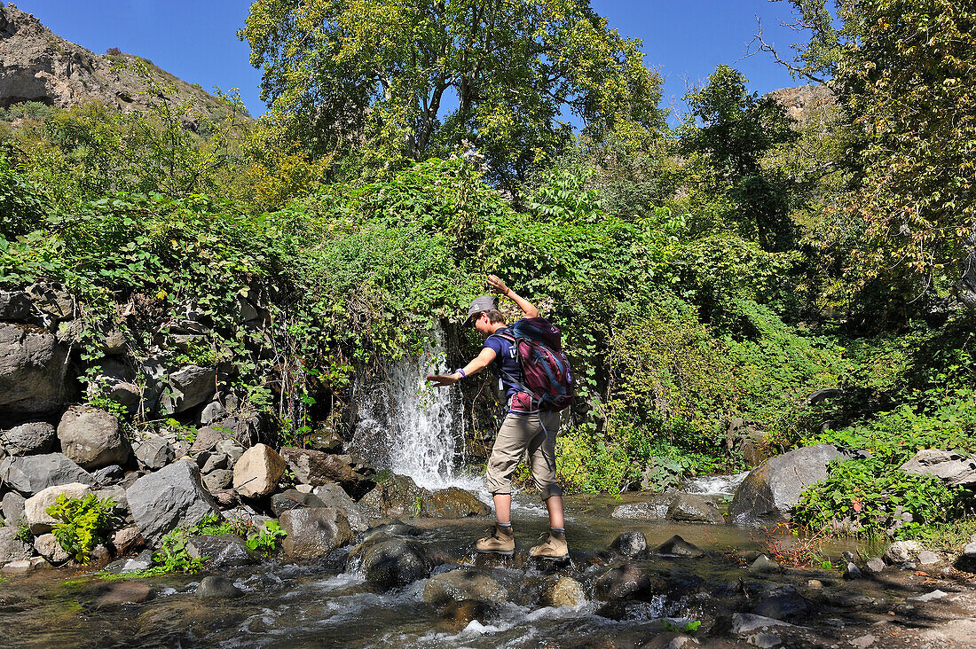 Hiker fording a stream near the deserted village of Old Shinuhayr in the Gorges of the Vorotan River, Syunik region, Armenia, Eurasia