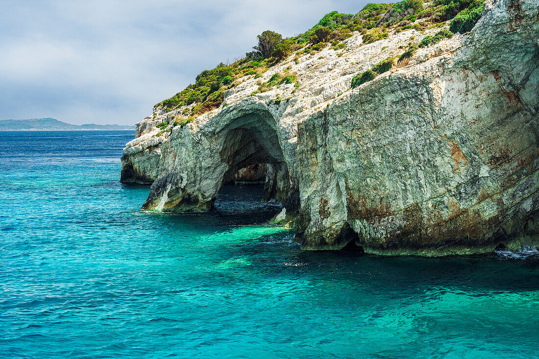 Natürliche Höhlenformation auf einem felsigen Hügel mit grüner Bepflanzung, die sich bis zum Meer erstreckt, Zakynthos, Ionische Inseln, Griechische Inseln, Griechenland, Europa