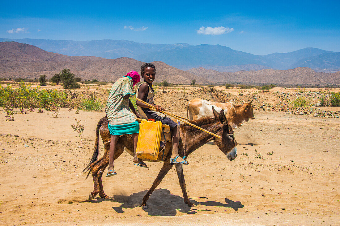 Boy and girl riding on a donkey to a waterhole in the lowlands of Eritrea, Africa