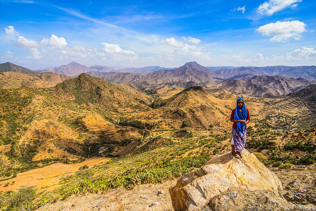 Einheimische Frau steht auf einem Felsen in schöner Berglandschaft entlang der Straße von Massawa nach Asmara, Eritrea, Afrika