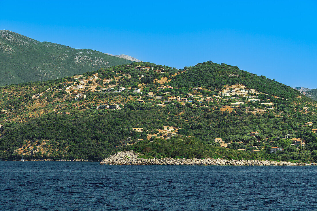 Sea view of low rise houses on the hill and close to the beach surrounded by green forest, Lefkada, Ionian Island, Greek Islands, Greece, Europe