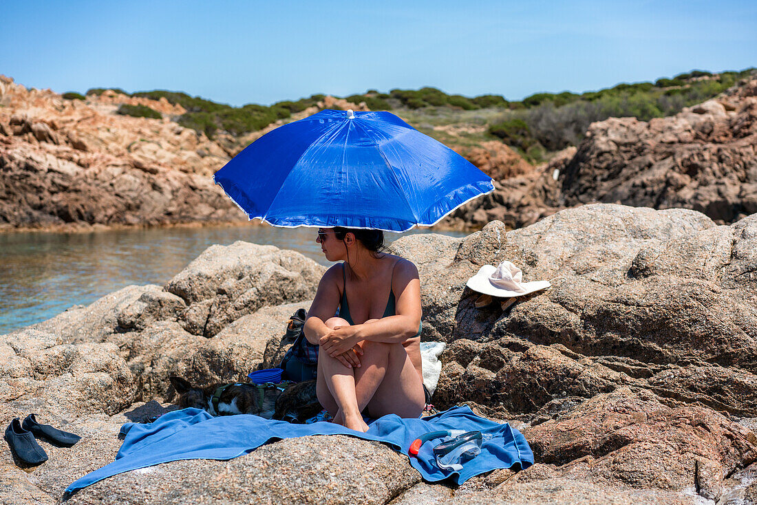 Frau mit Hund unter einem Sonnenschirm an einem Strand, Sardinien, Italien, Mittelmeer, Europa