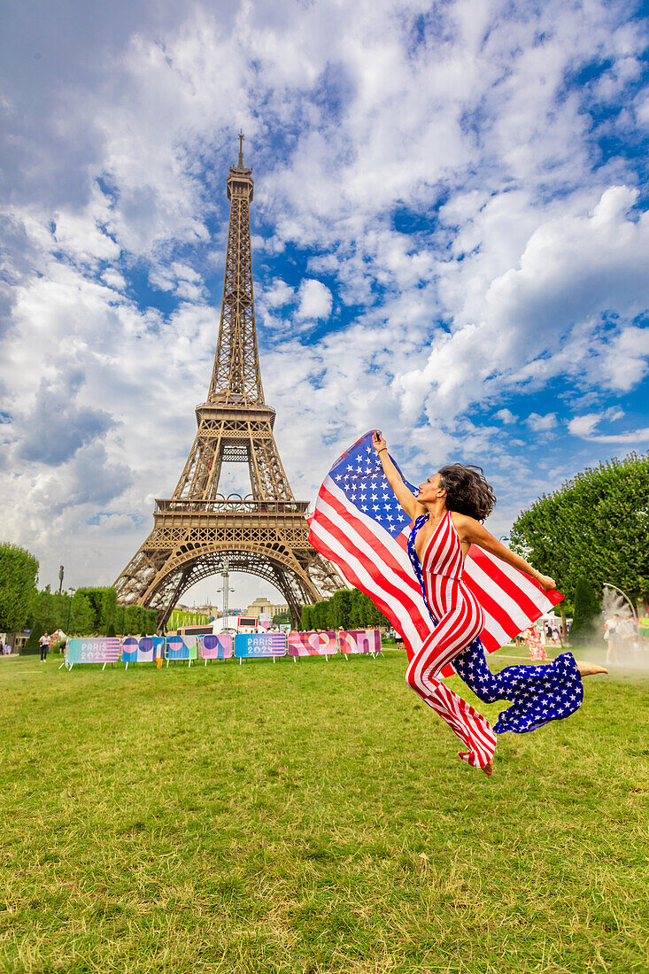 Patriotic American Woman jumping and cheering for Team USA and the Paris 2024 Olympics in front of the Eiffel Tower, Paris, France, Europe