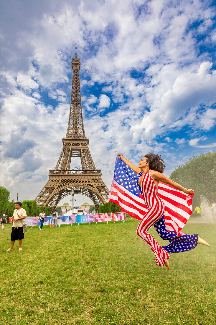 Patriotische amerikanische Frau springt und jubelt für das Team USA und die Olympischen Spiele Paris 2024 vor dem Eiffelturm, Paris, Frankreich, Europa